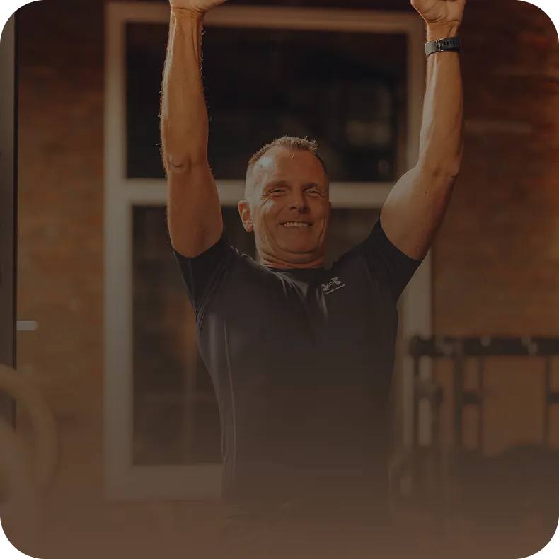 Mann beim Training mit erhobenen Armen im Peoples Fitness Studio – Freude und Motivation