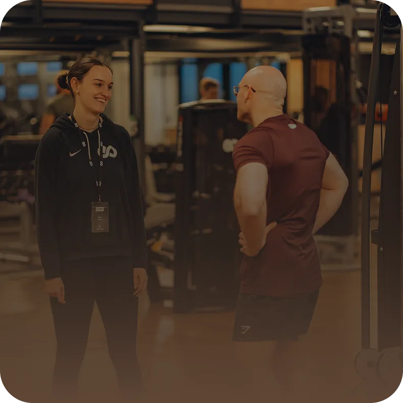 Peoples Trainerin im Gespräch mit einem Mitglied auf der Trainingsfläche – persönliche Betreuung